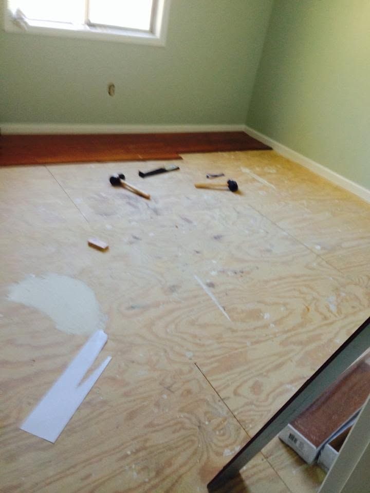 Partially stripped bedroom floor with tools and plywood underlayment, near a window and green walls
