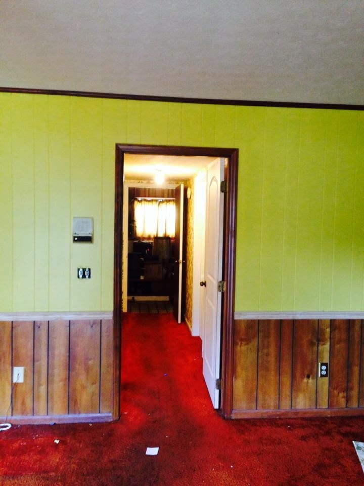 Old hallway with red carpet, yellow walls, and an open doorway to a brighter room