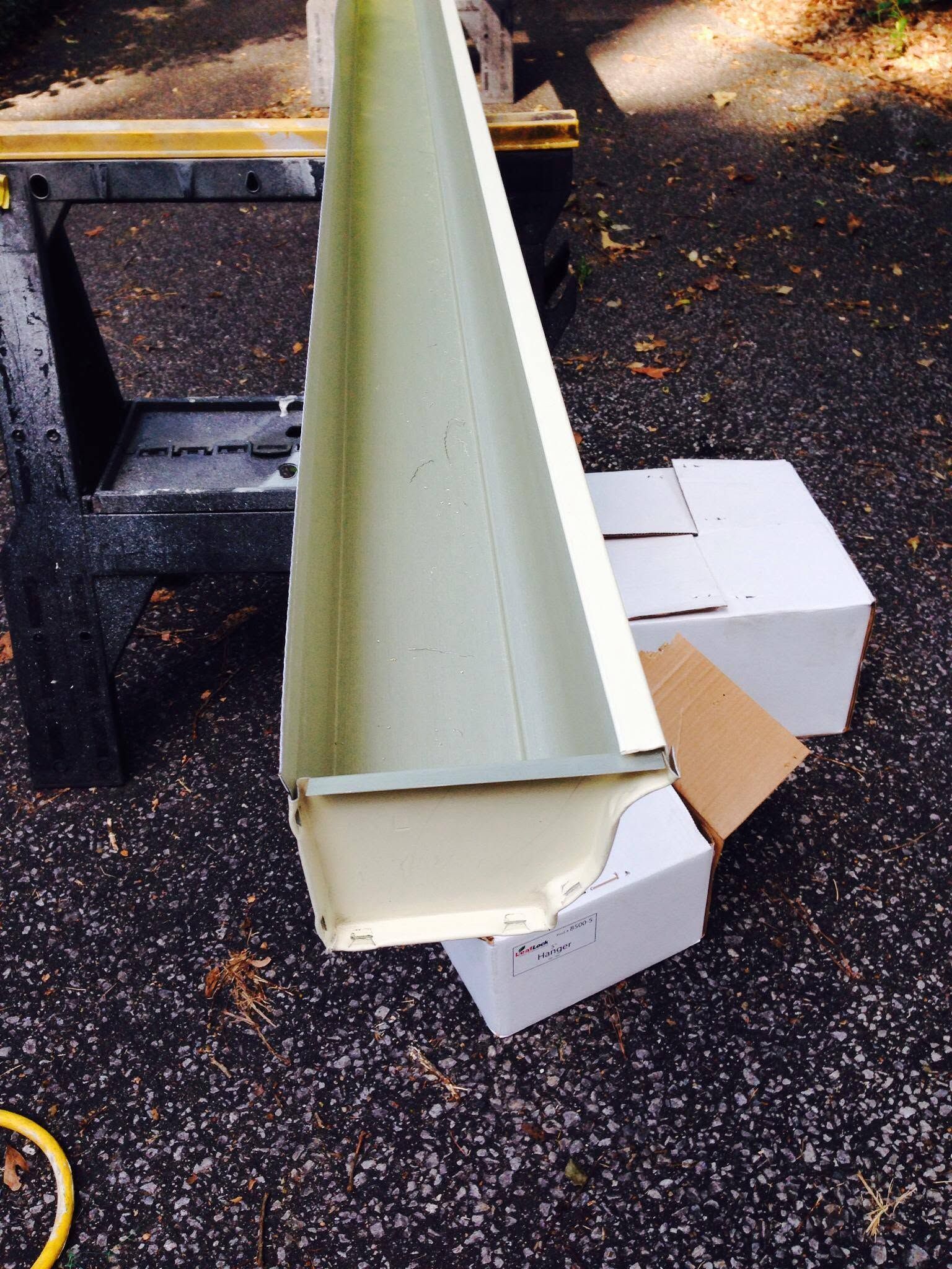 Long green metal gutter resting on white boxes outdoors on asphalt.