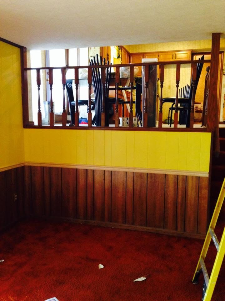 Empty room with yellow walls, wood paneling, red carpet, and a railing overlooking stacked chairs
