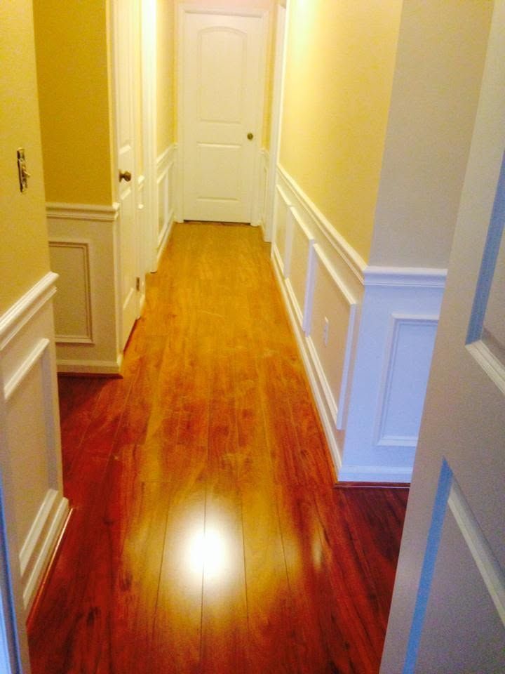 Narrow hallway with yellow walls, white trim, and polished hardwood floor leading to a closed white door.