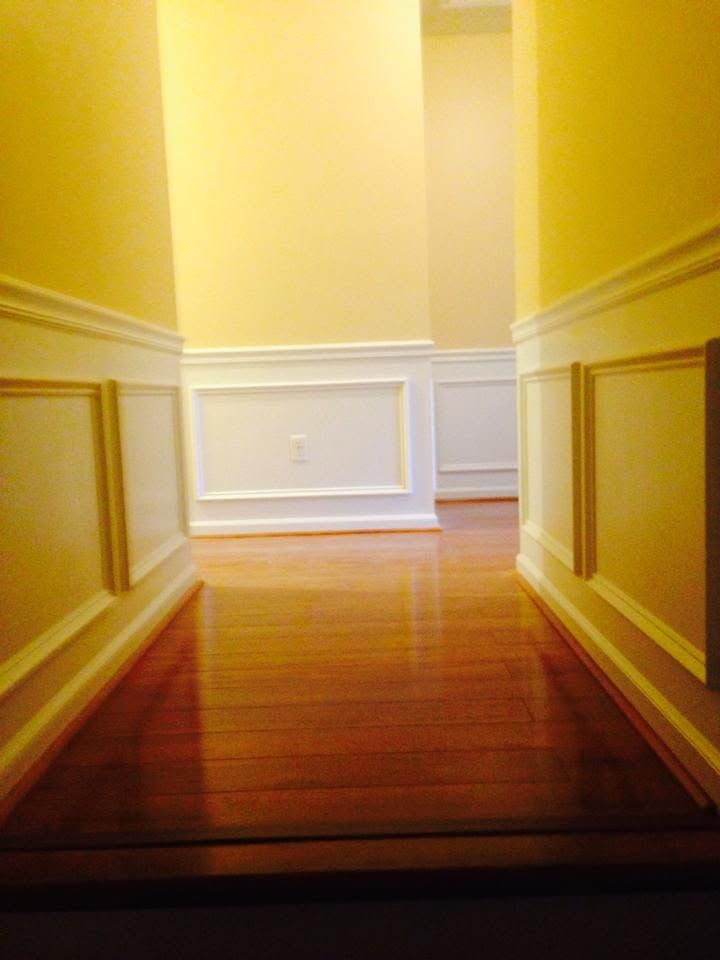 Empty hallway with yellow walls, white trim, and a polished wooden floor