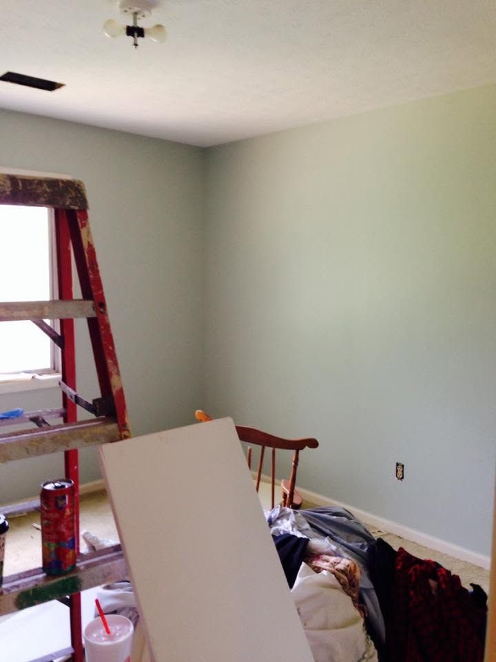 Partially renovated room with pale green walls, ladder by window, and cluttered furniture in the foreground