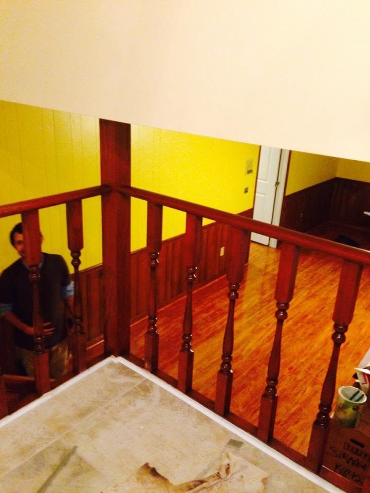 Indoor staircase with wooden railing, yellow walls, and a person seated on the left side.