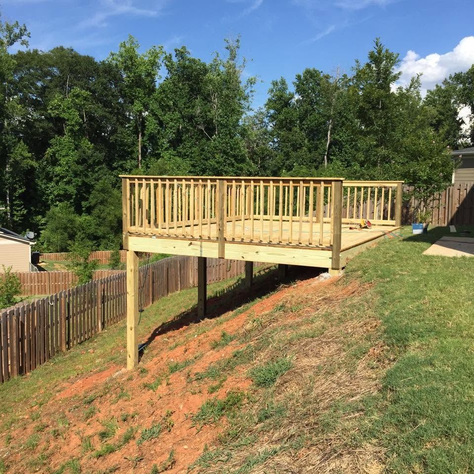 Wooden deck built on a steep grassy hillside beside a fence and trees