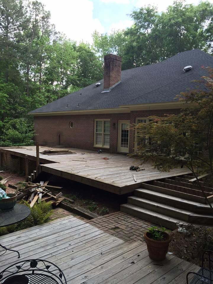 Wooden backyard deck beside a house, with steps, potted plants, and trees surrounding it.