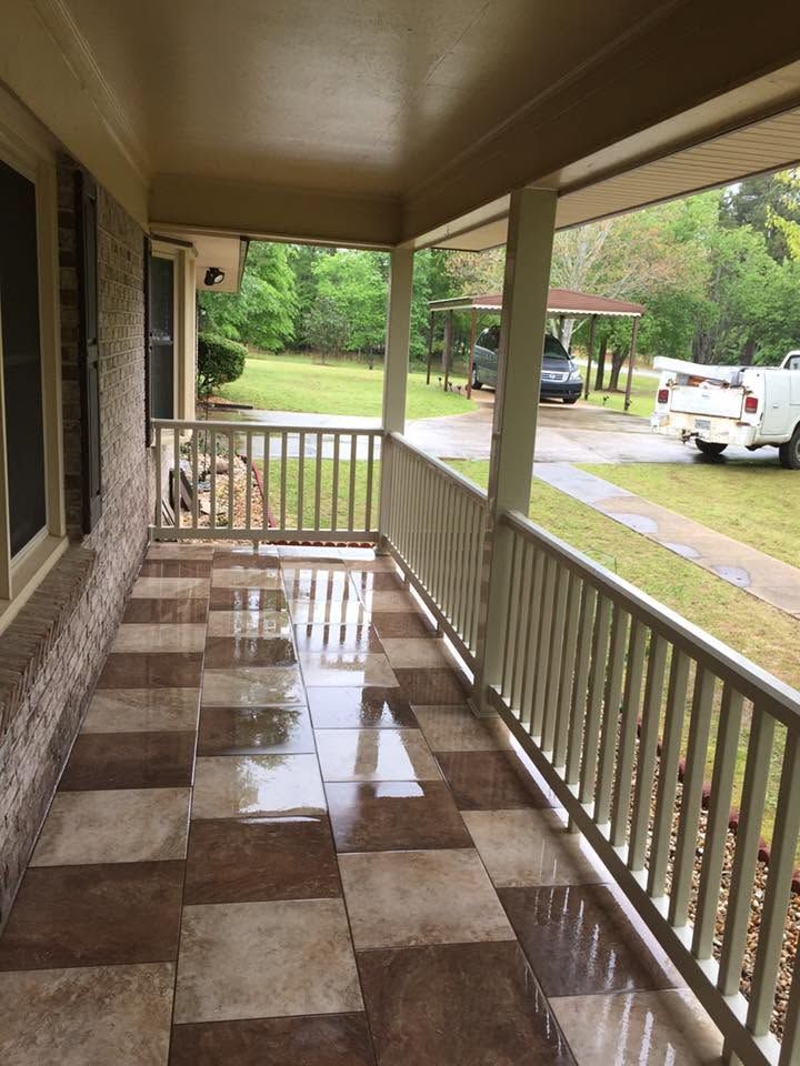 Covered porch with checkered tile floor, white railing, and a view of a driveway and trees.