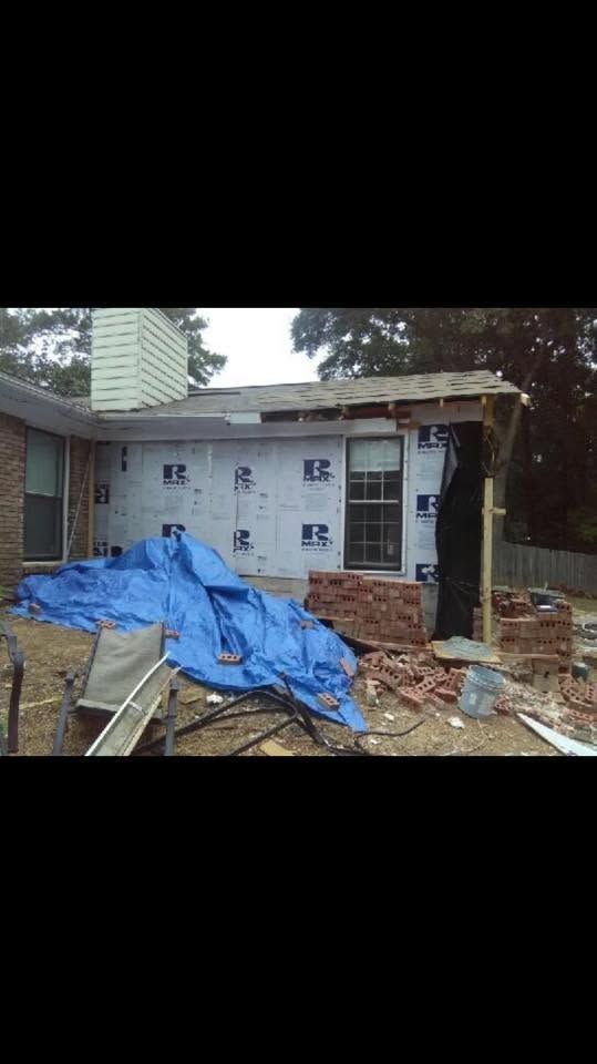 House under renovation with white siding, blue tarp, and scattered construction debris in front.