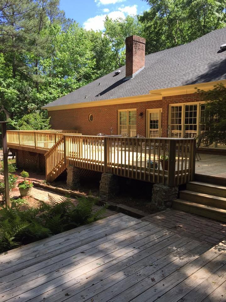 Wooden house with wraparound deck and stairs, surrounded by trees and greenery
