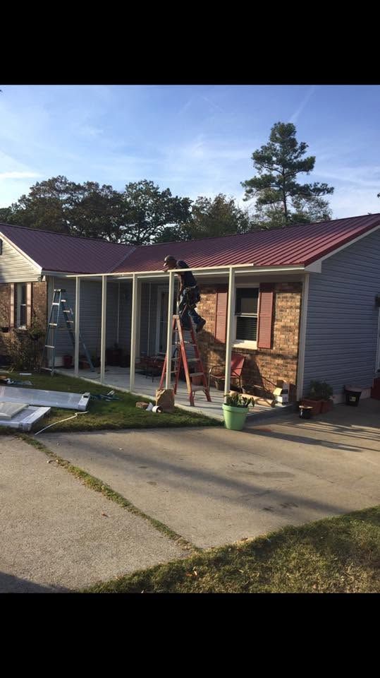 Worker on a ladder painting the front of a single-story house with a red roof.