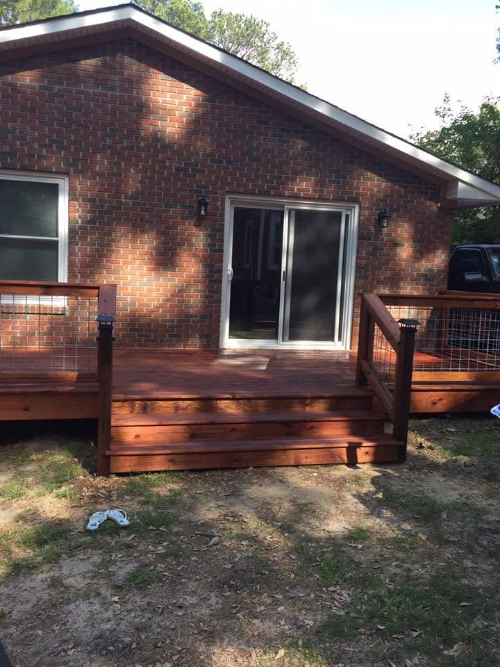 Brick house with sliding glass doors and a wooden deck in a shaded yard