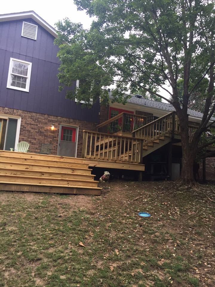 Backyard deck and stairs beside a blue house, with a large tree and one person crouching underneath.