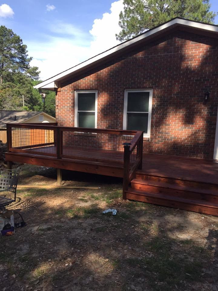 Brick house with a wooden deck and steps in a wooded yard.