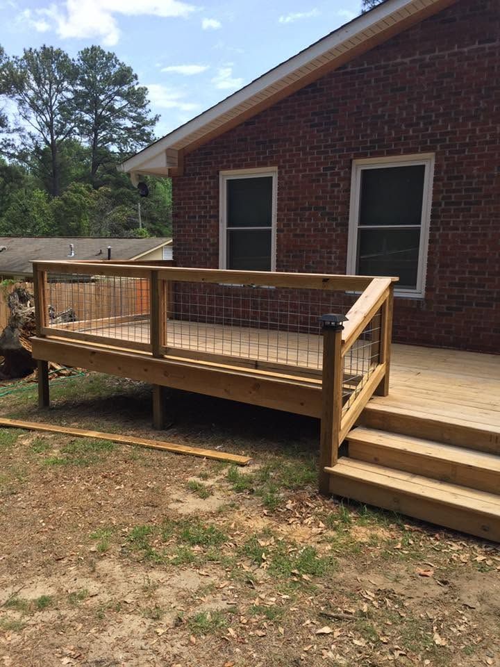Wooden ramp and deck attached to a brick house with two windows and stairs leading down to the yard