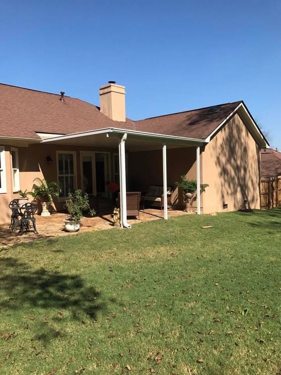 Backyard view of a brick house with a covered patio, lawn, and clear blue sky