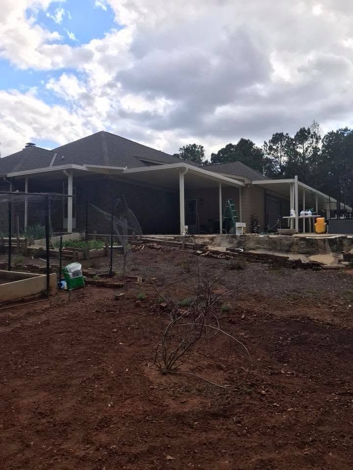 House under construction with a dark roof, unfinished dirt yard, and cloudy sky.