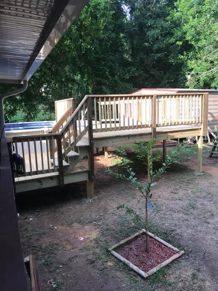 Wooden backyard deck with railing and steps beside a house, overlooking a small planted sapling below.