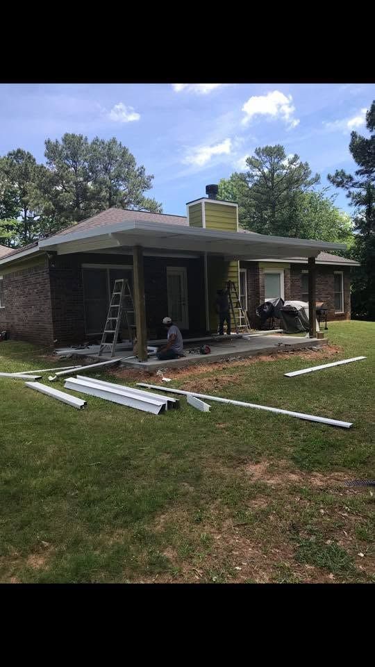 Brick house under renovation with ladders, roofing materials, and debris in the yard