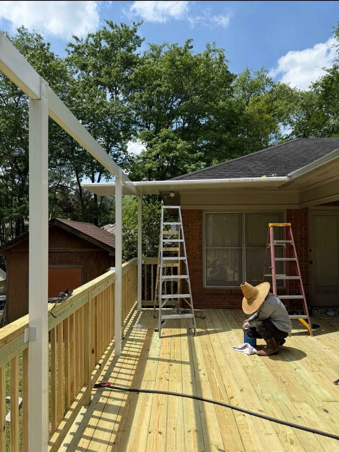 Workers painting a wooden deck beside a house, with ladders and white railing posts.