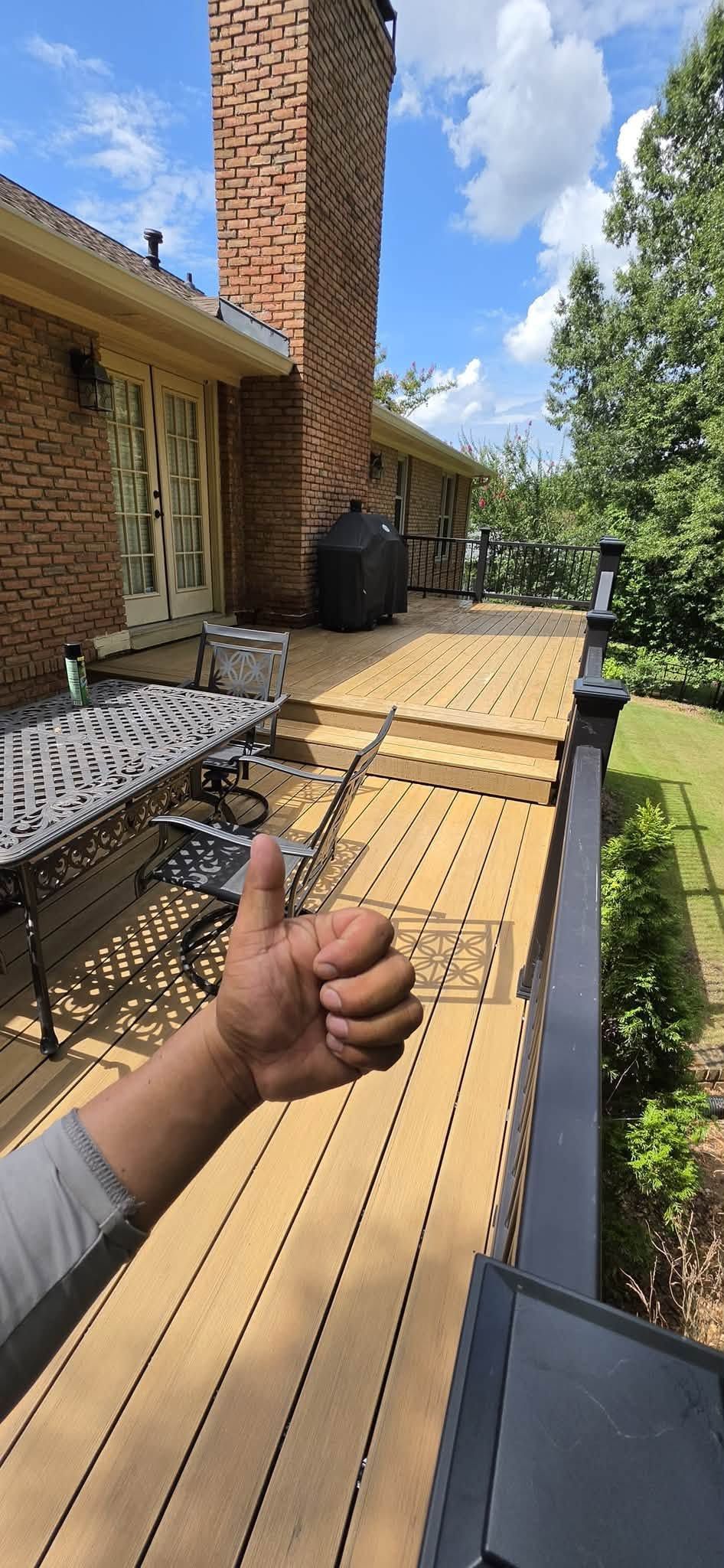 Thumbs-up gesture beside a wooden ramp leading to a brick house on a sunny day