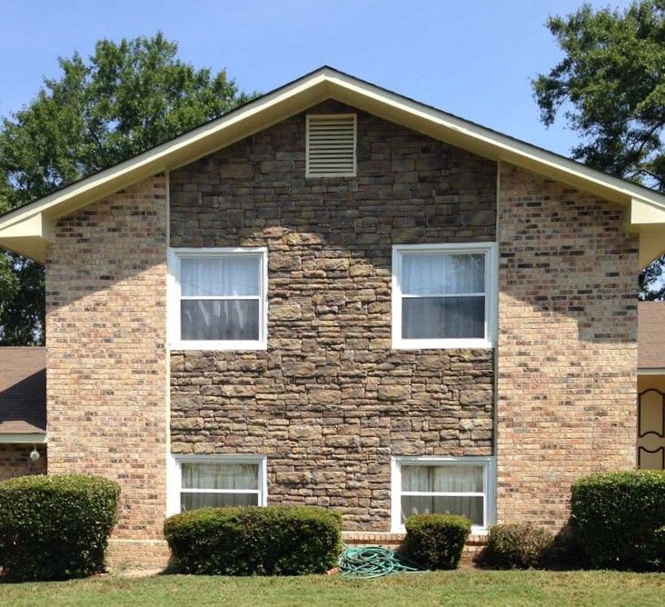 Two-story brick apartment building with tan siding, white windows, and trimmed bushes in front