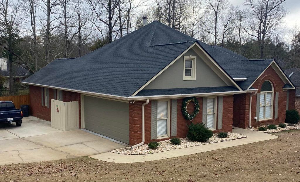 Suburban brick house with gray roof, beige garage, and front porch surrounded by bare trees