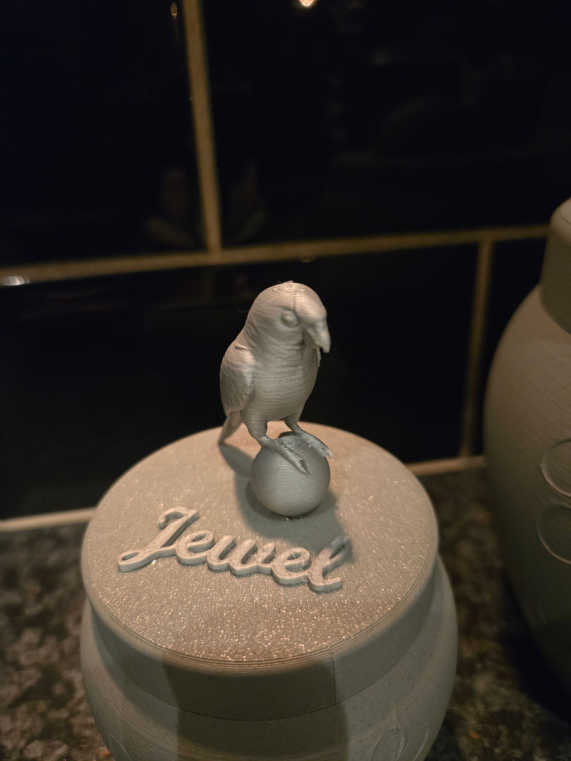 Een lichtgrijze, glinsterende urn, versierd met een klein vogeltje en de naam 