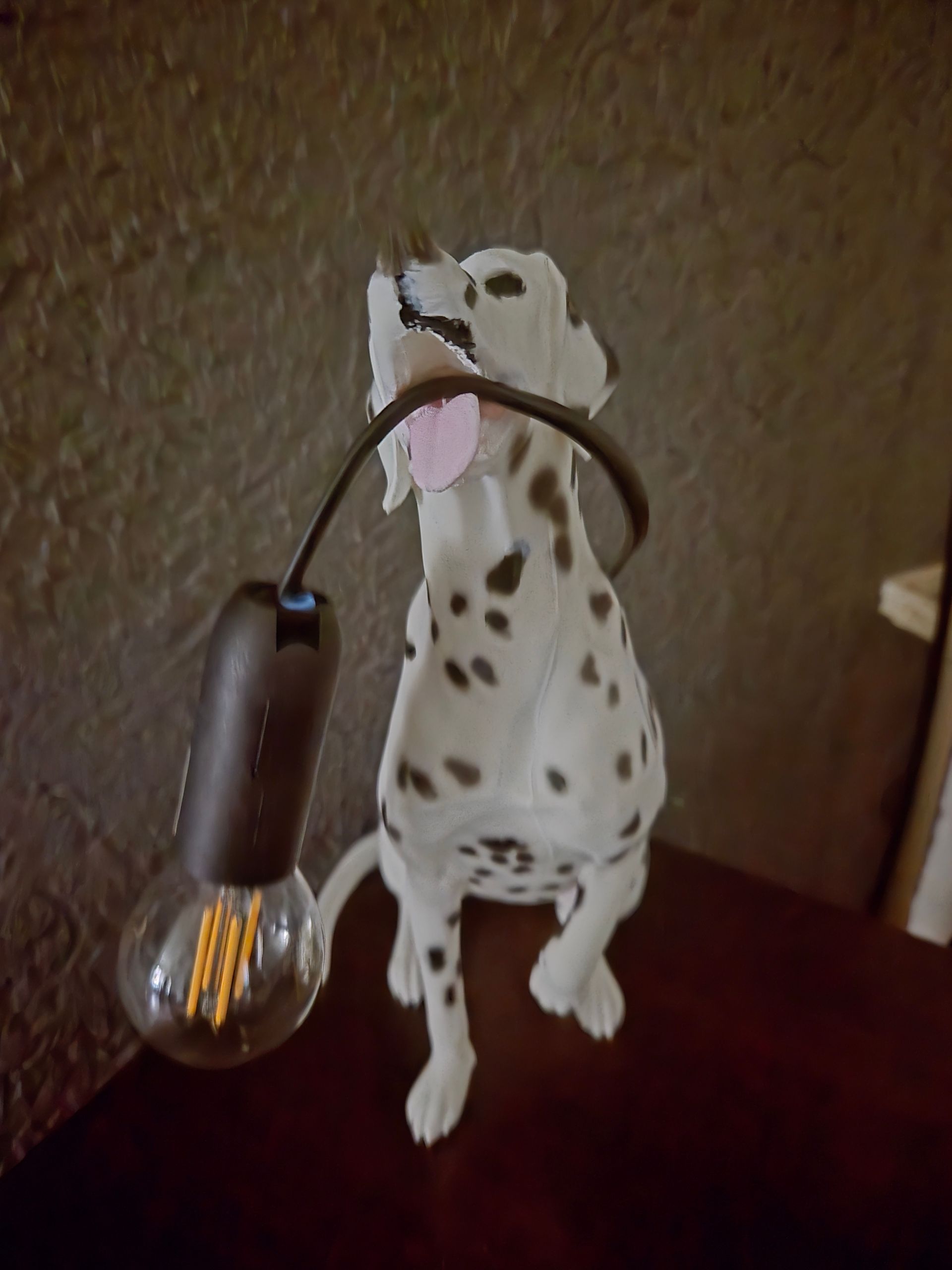 Een decoratief Dalmatiërbeeldje houdt een hanglamp met een Edison-lamp in zijn bek, geplaatst op een donkerhouten ondergrond.