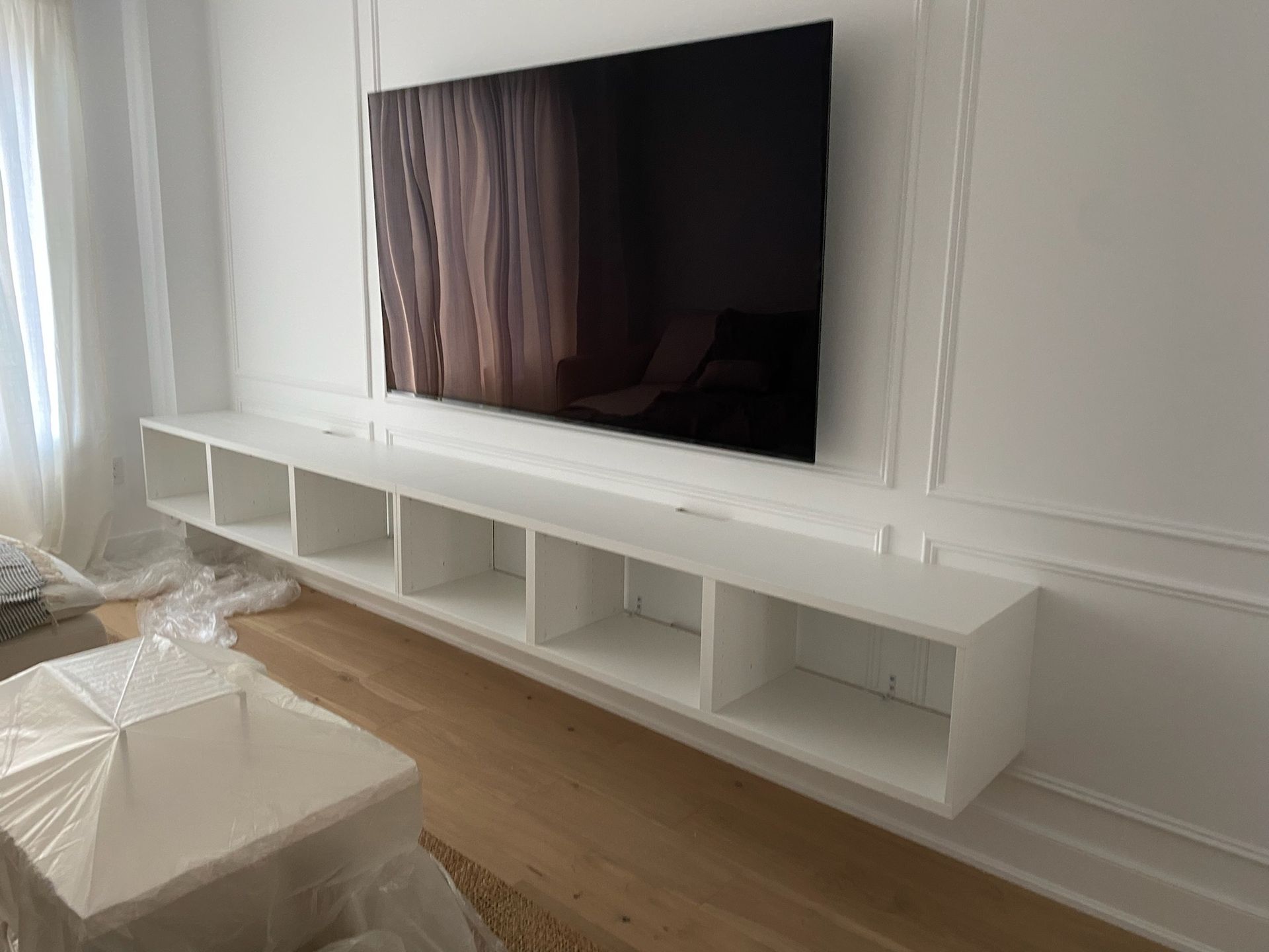 White floating shelf unit beneath a wall-mounted TV on a white wall.