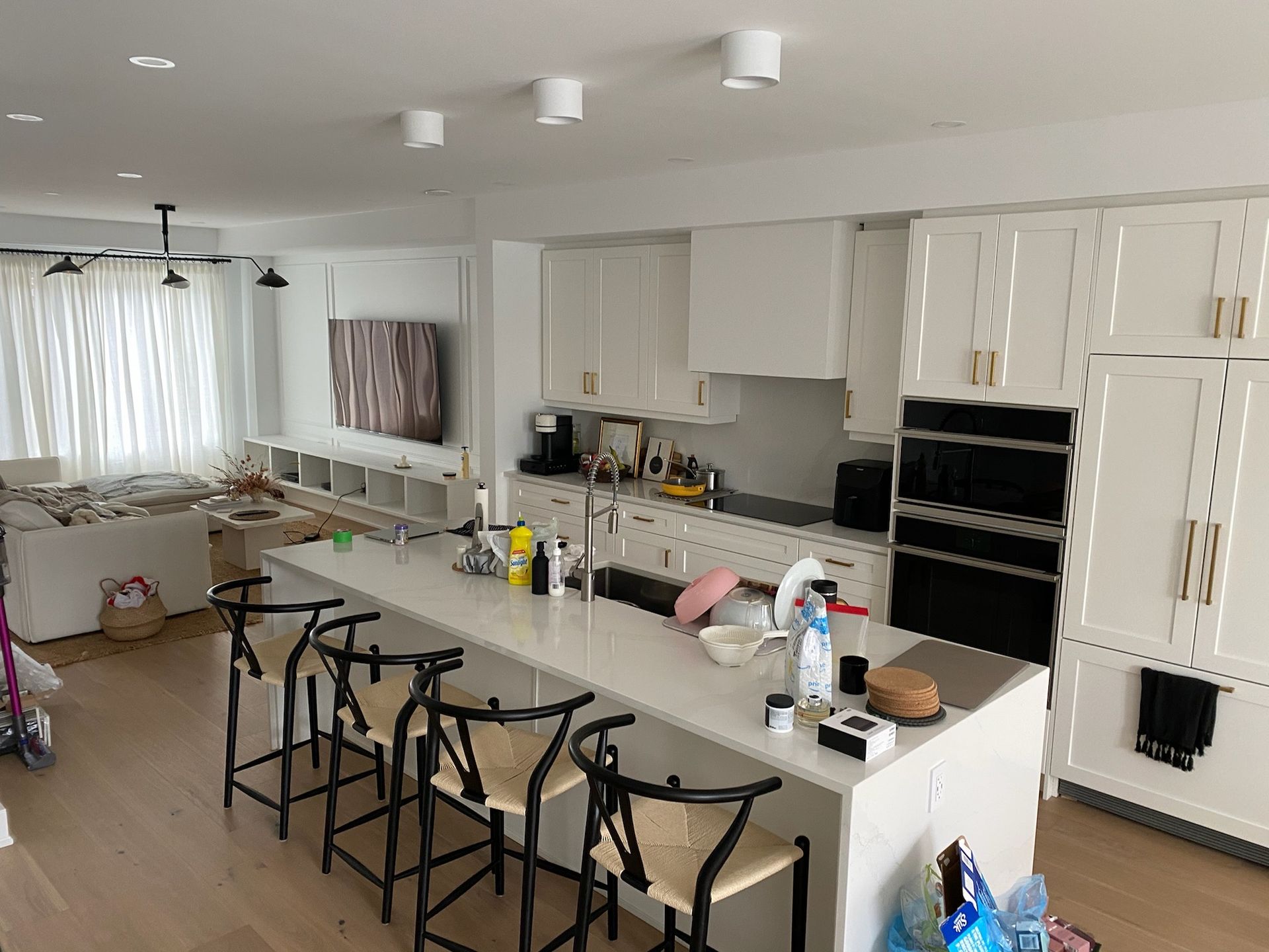 Kitchen with white cabinets, island with stools, and built-in ovens.