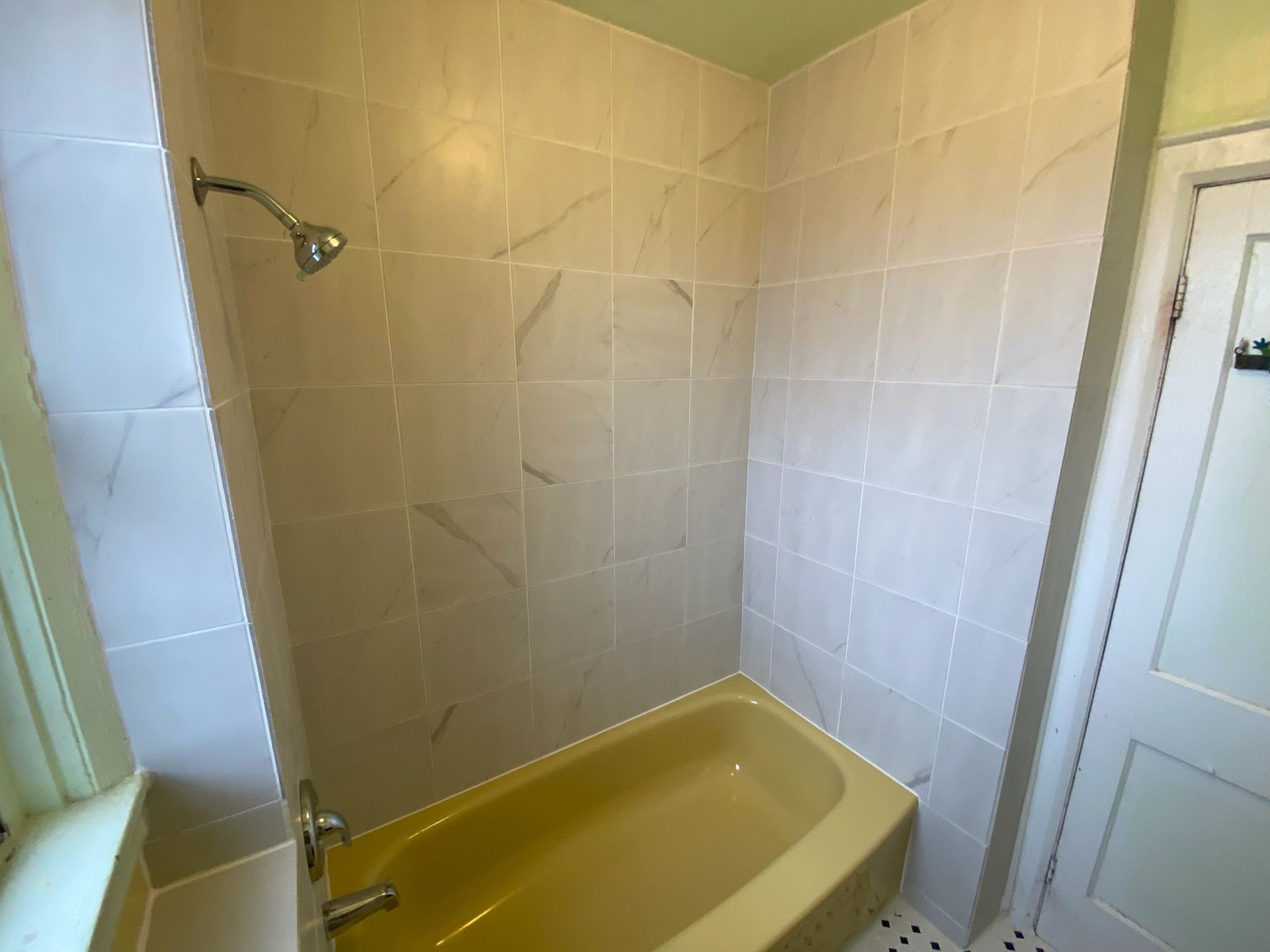 Yellow bathtub and tile shower with a shower head in a bathroom.