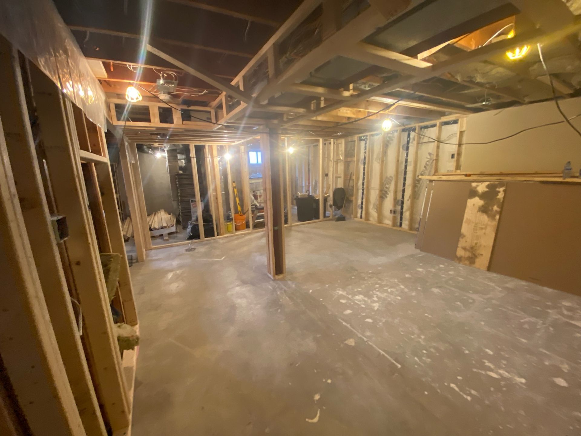 Basement interior during renovation, with exposed framing, concrete floor, and scattered debris.