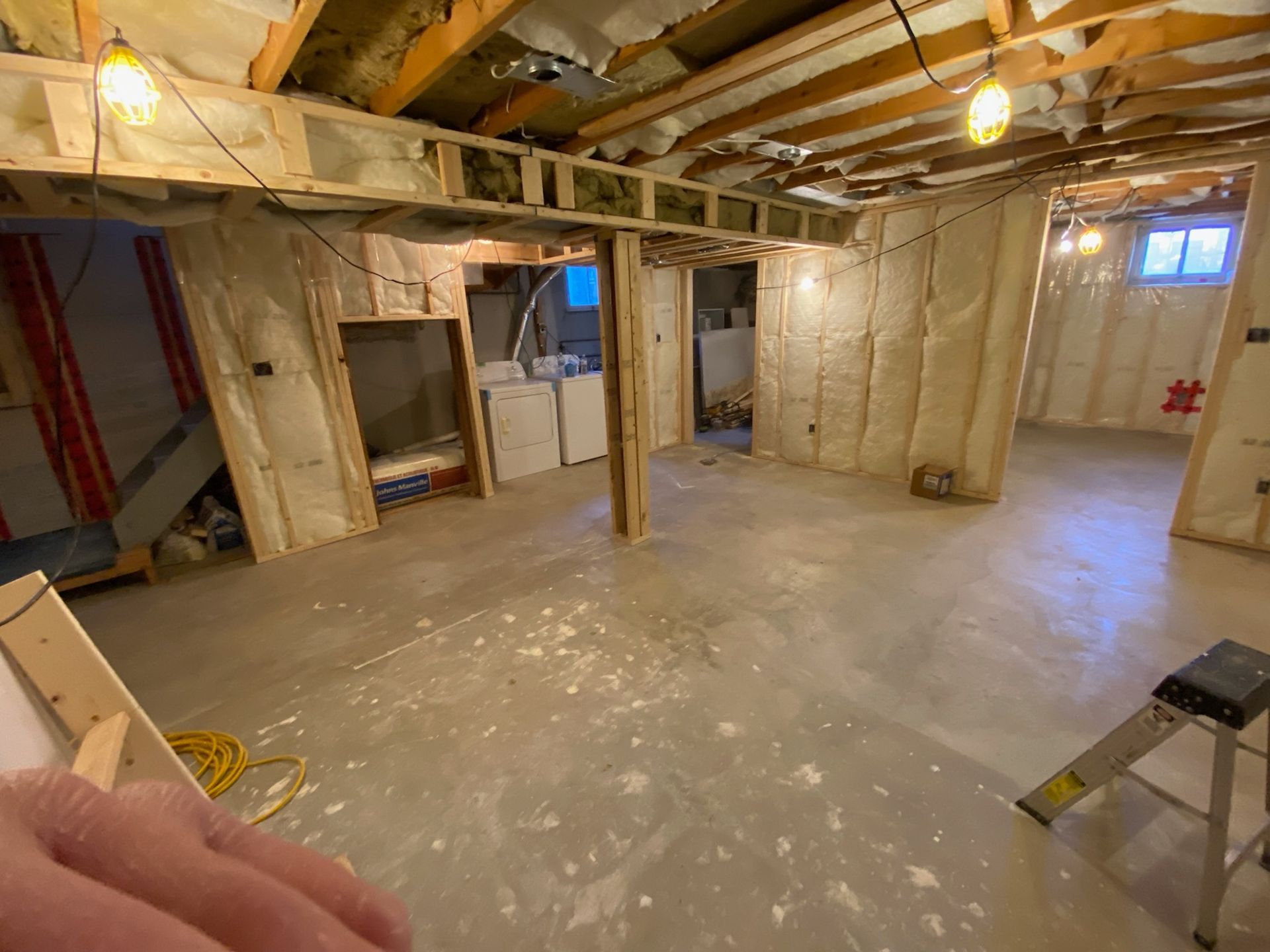 Basement under renovation with exposed insulation, framing, and unfinished concrete floor.