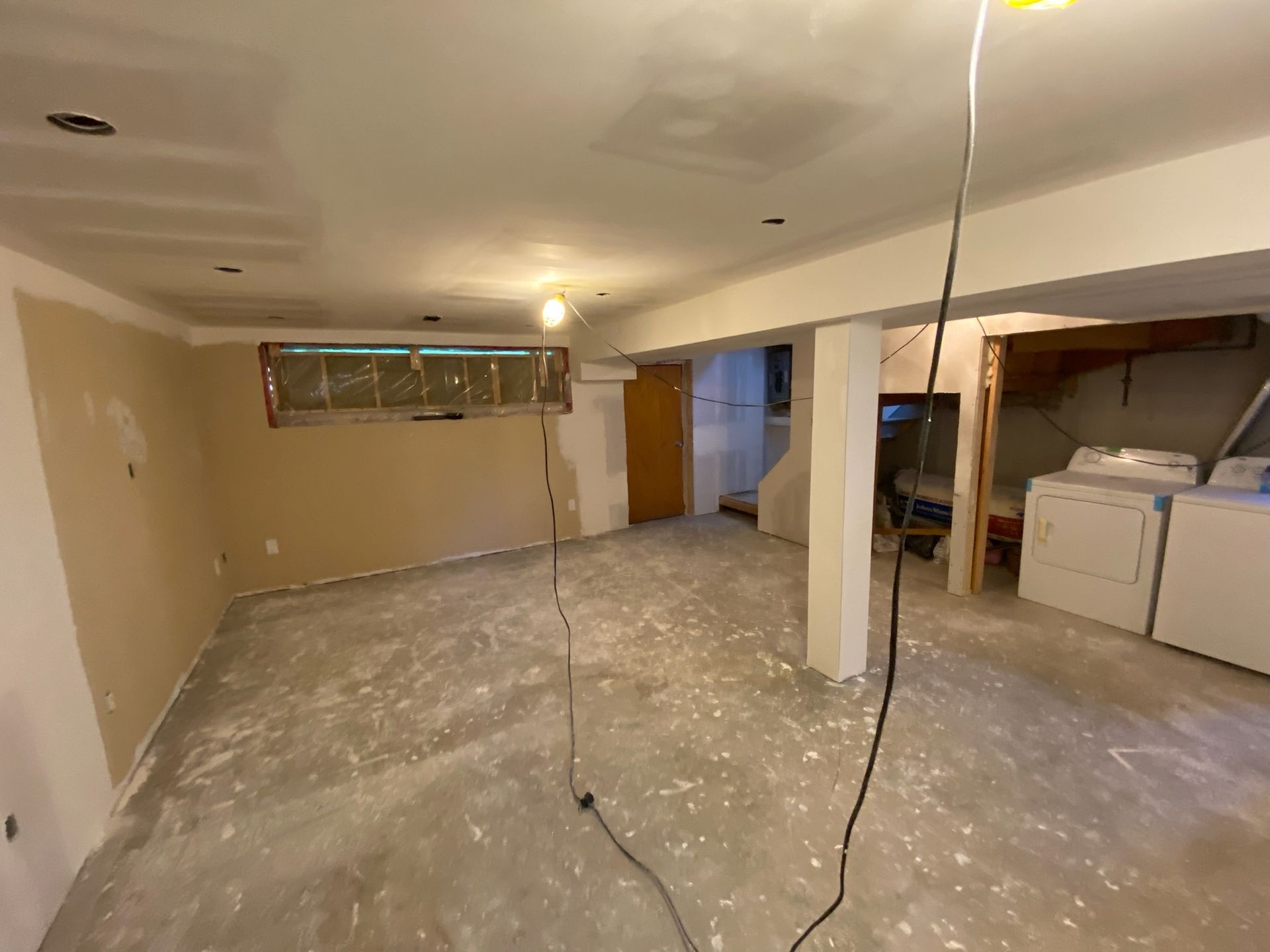 Basement renovation in progress; exposed concrete floor, drywall, unfinished walls, washer/dryer in the background.