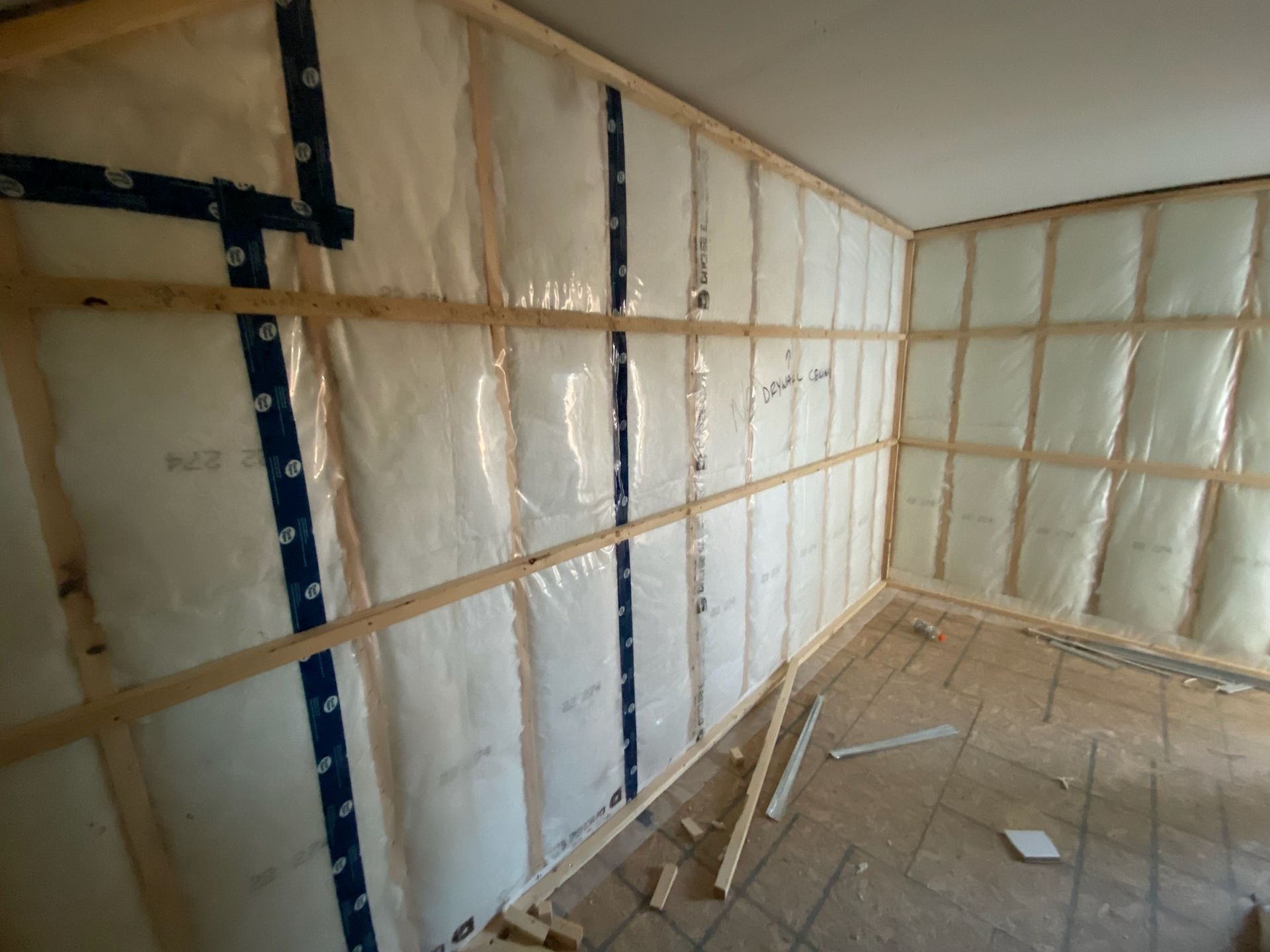 Interior wall framing with insulation wrapped in plastic, ready for drywall.
