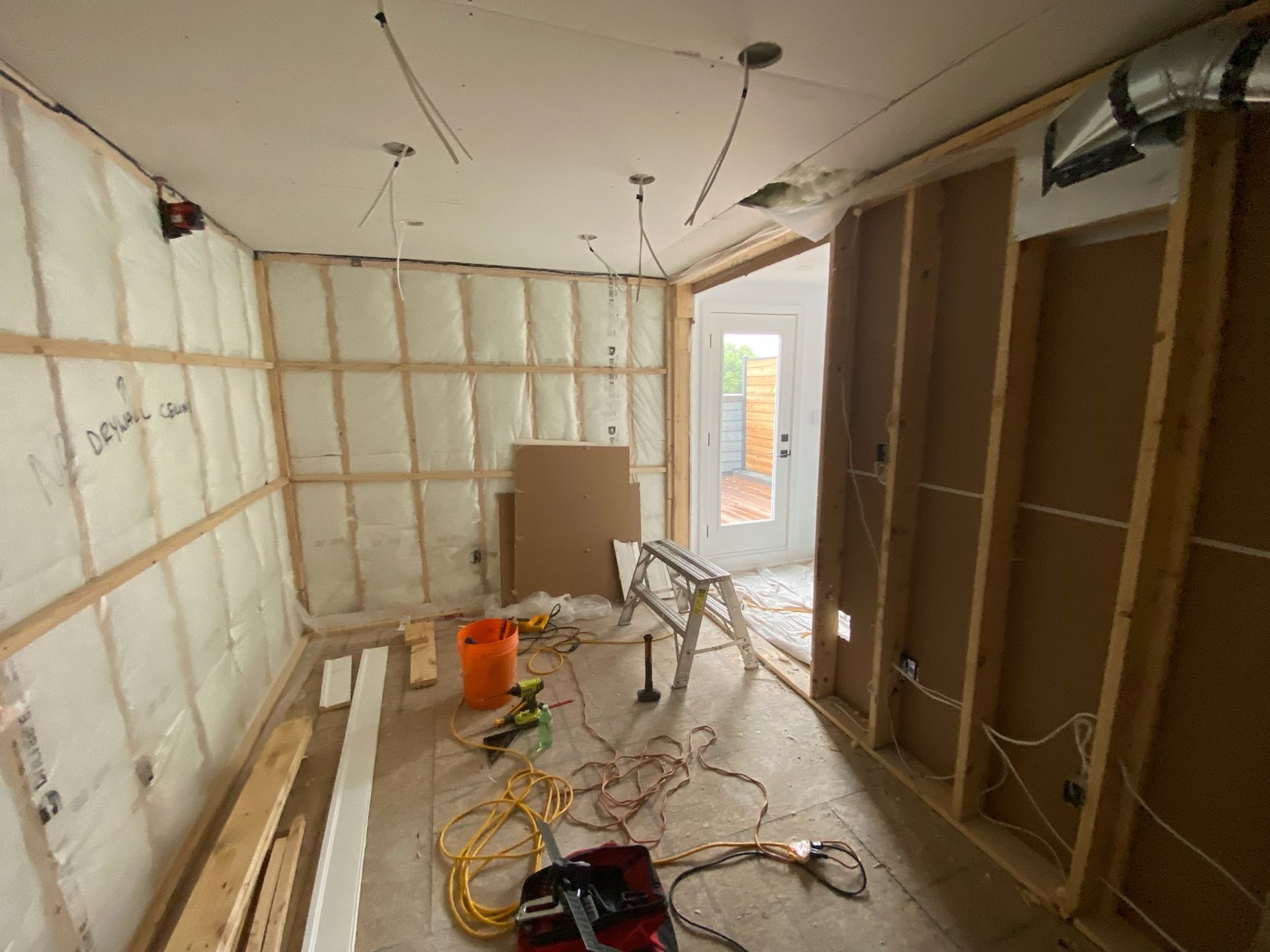 Room under construction: exposed framing, insulation, wiring, door to exterior. Construction tools scattered.