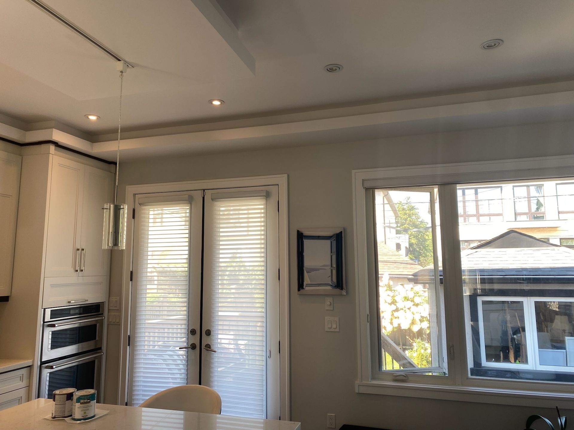 Interior view of a kitchen with light cabinets, a glass pendant lamp, and a window overlooking a building.