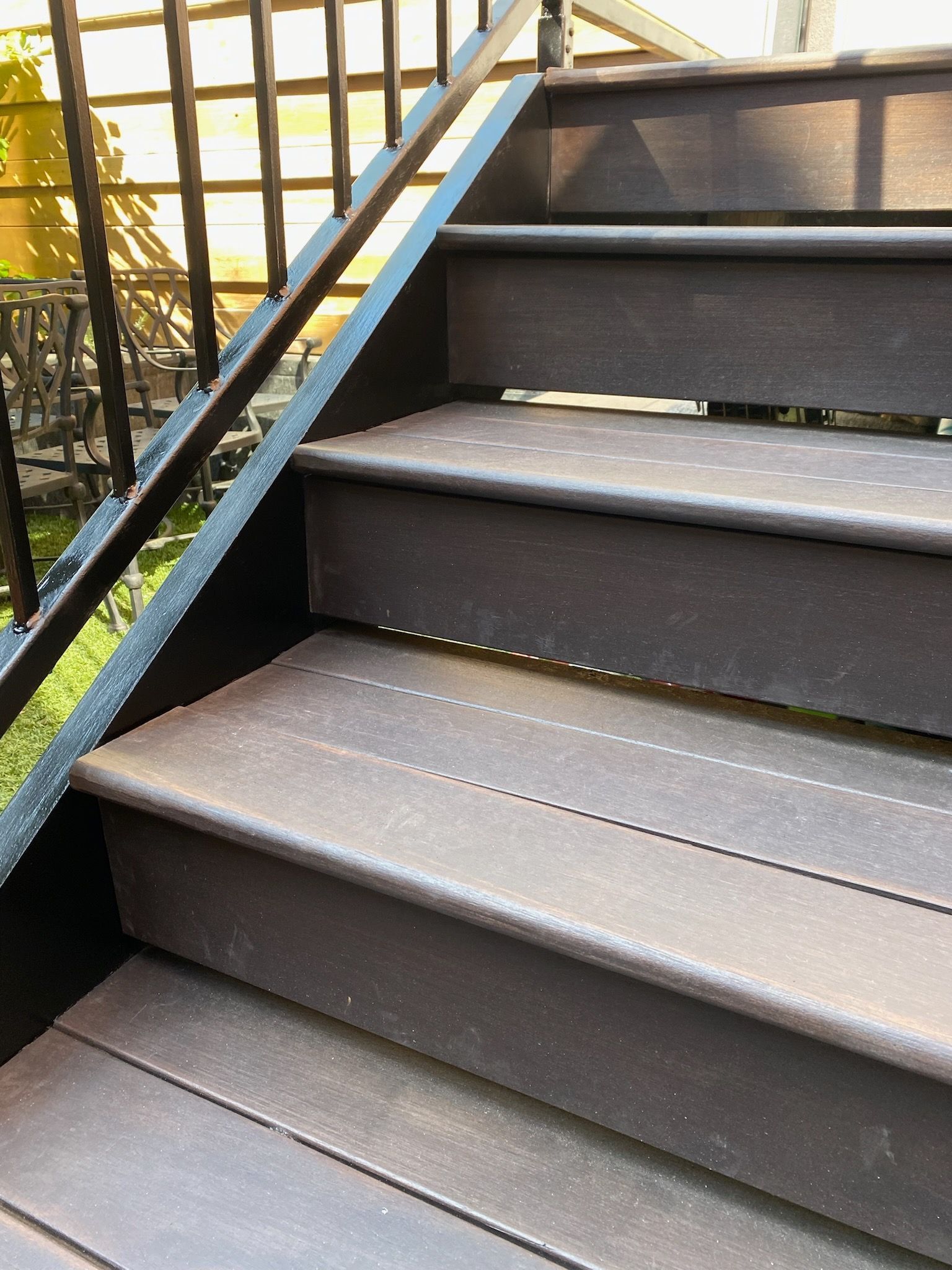 Dark brown composite stairs with a black metal railing.