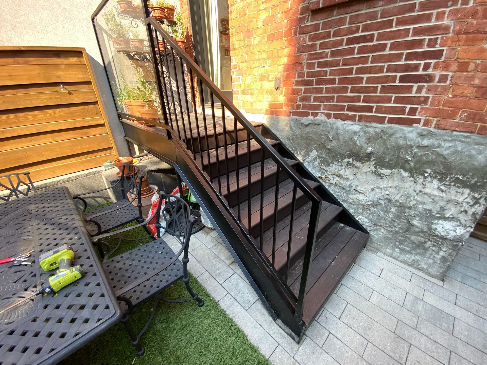 Black metal outdoor staircase with railing, wooden steps, and brick wall background.