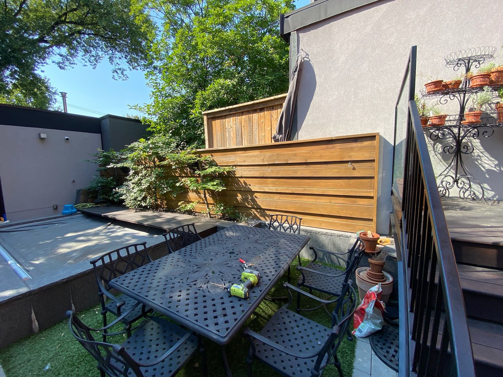 Patio with metal table and chairs, wooden fence, greenery, and building.