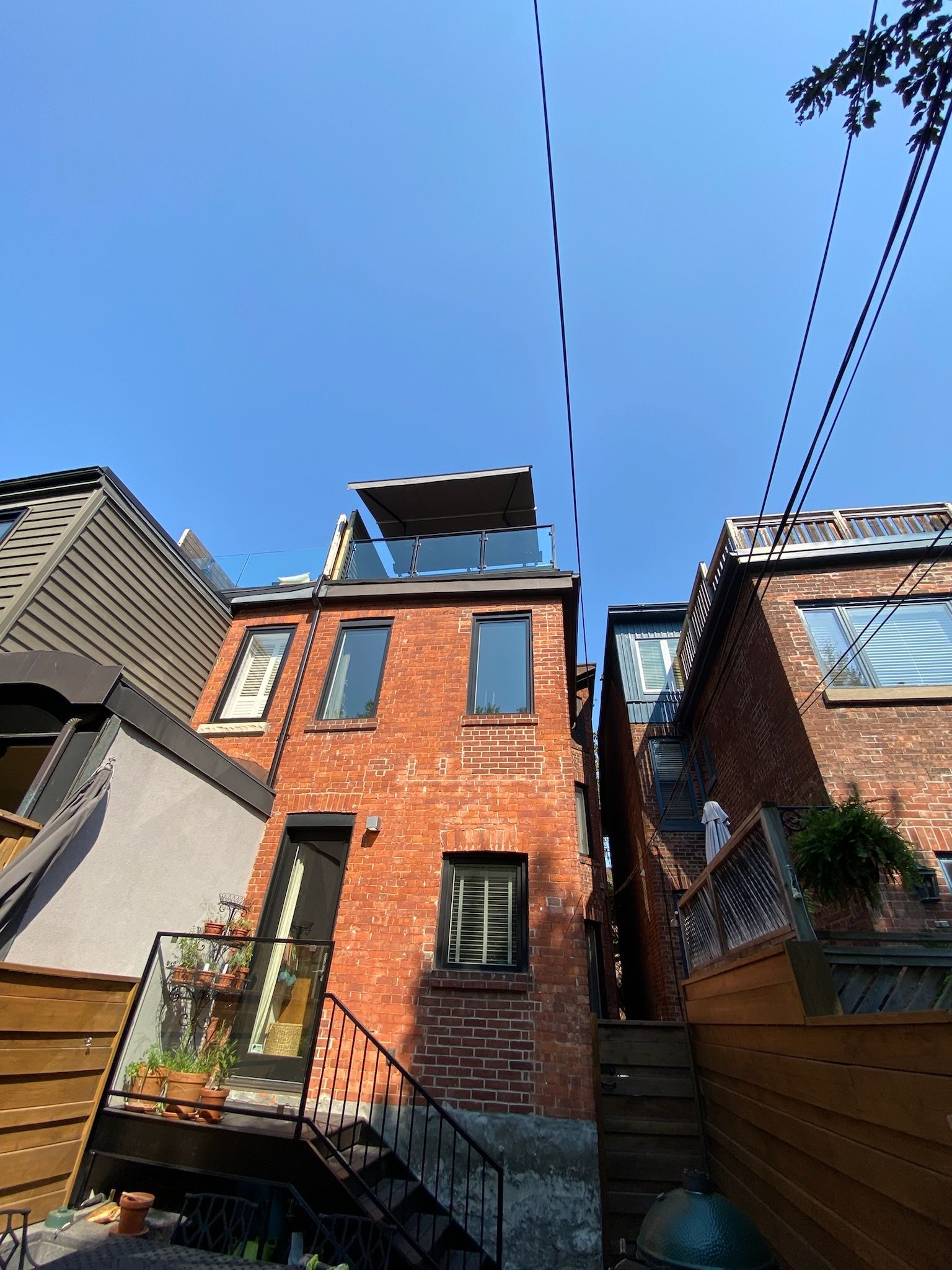 Brick house with black trim, rooftop patio, and exterior stairs, under a blue sky.