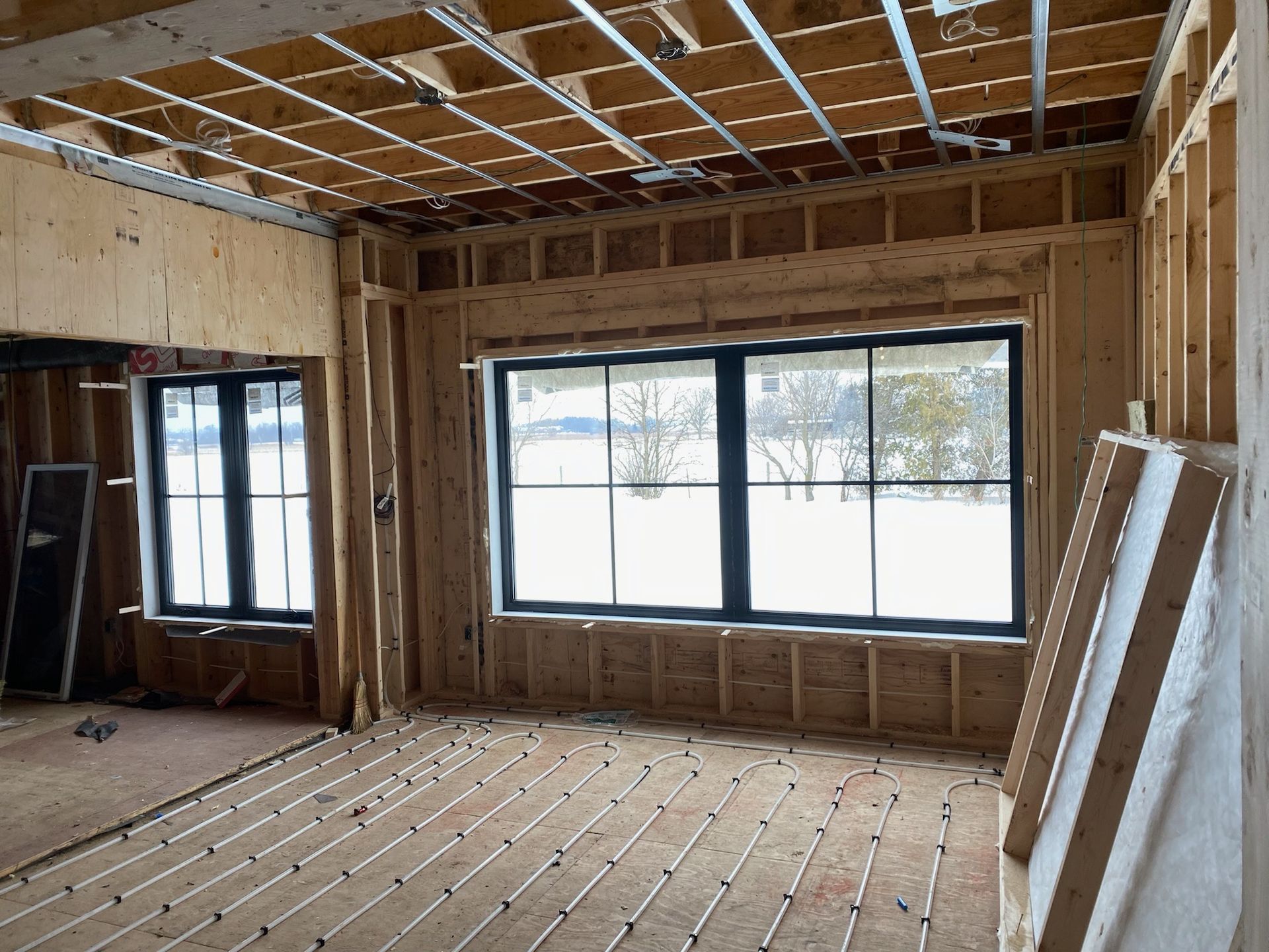 Interior of a room under construction, with wooden framing, windows, and snow visible outside.