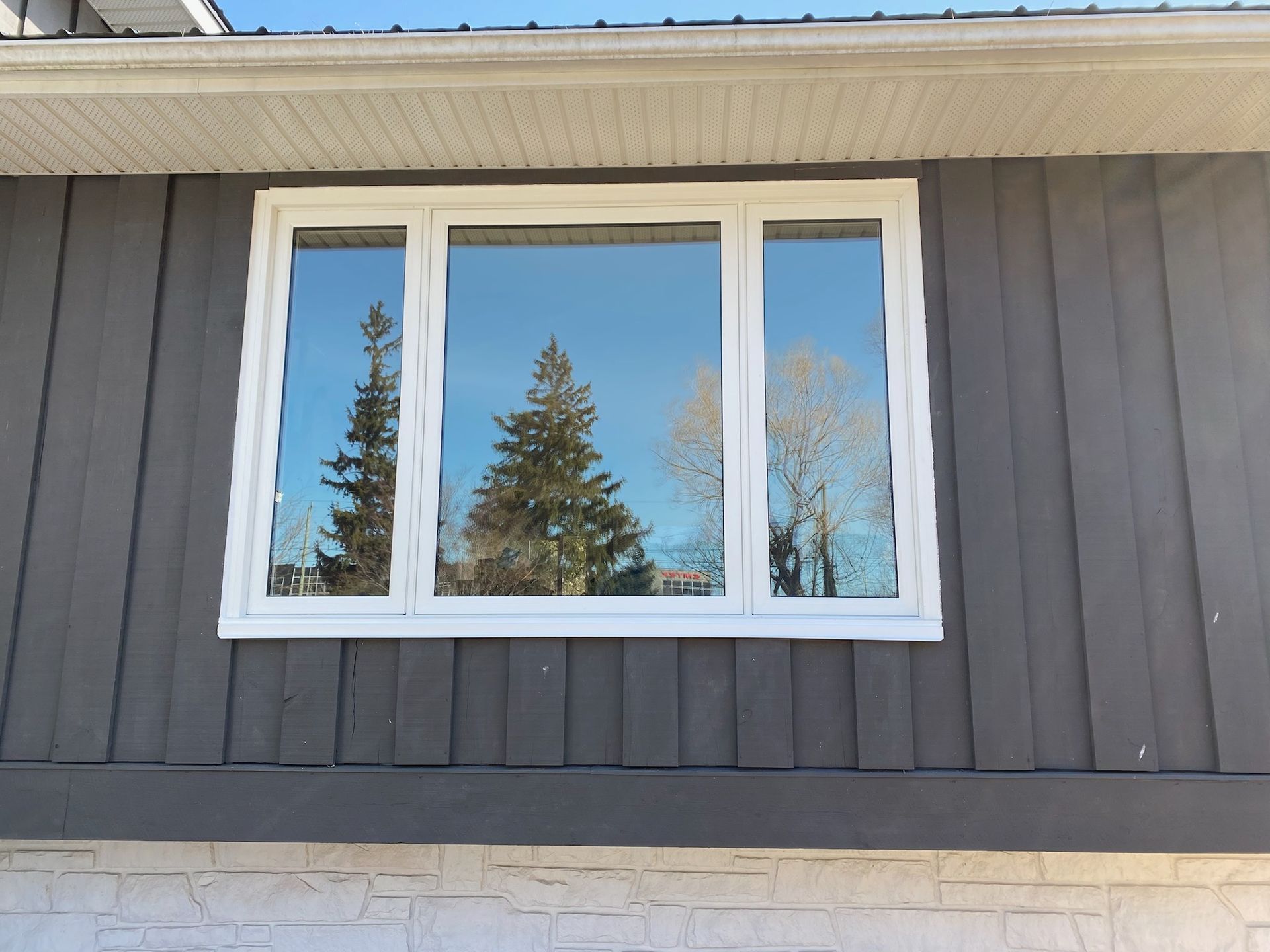 White-framed window on a gray building, reflecting trees and a blue sky.