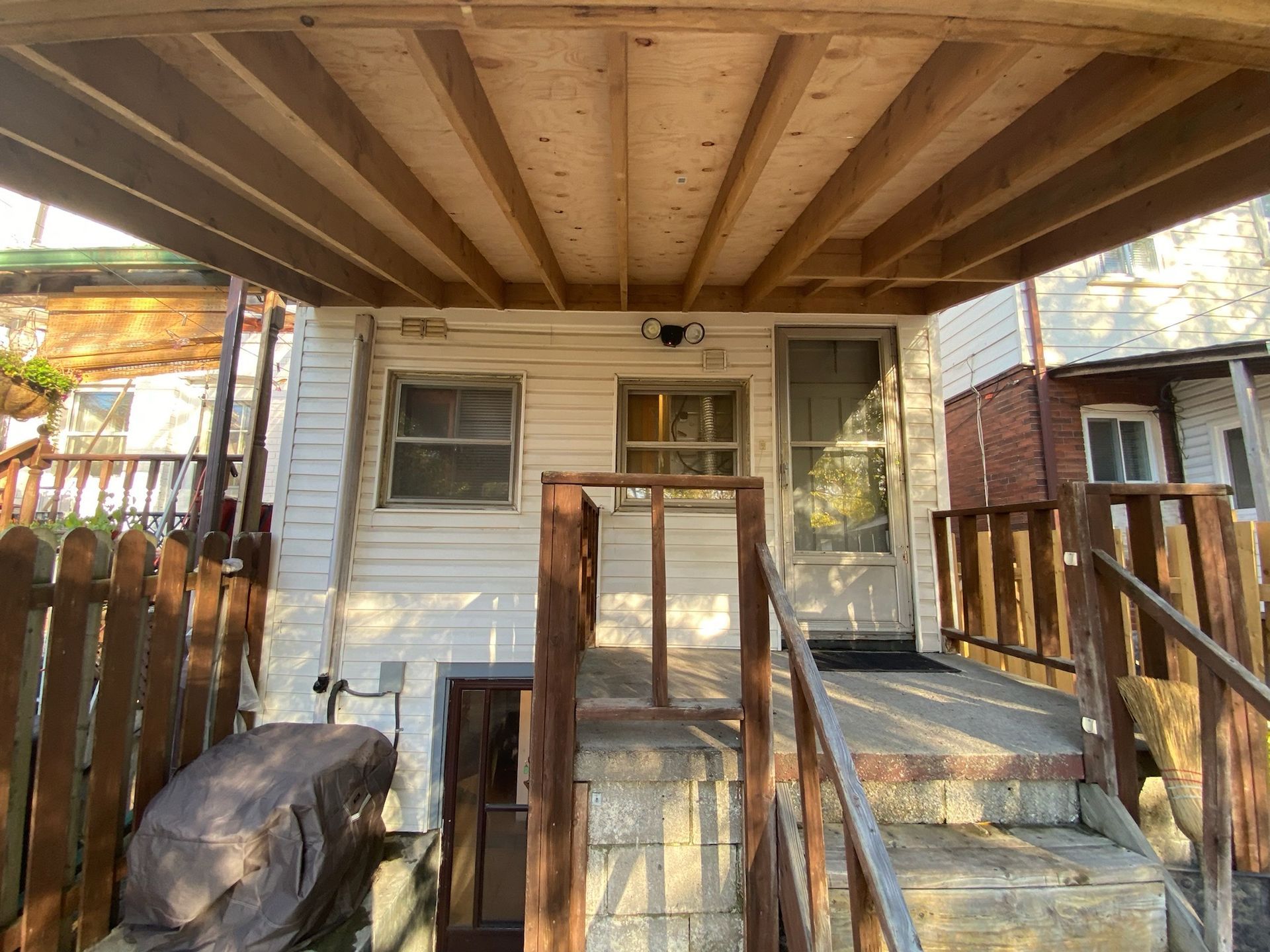 Back entrance with porch and steps, white siding, wooden fence and roof.