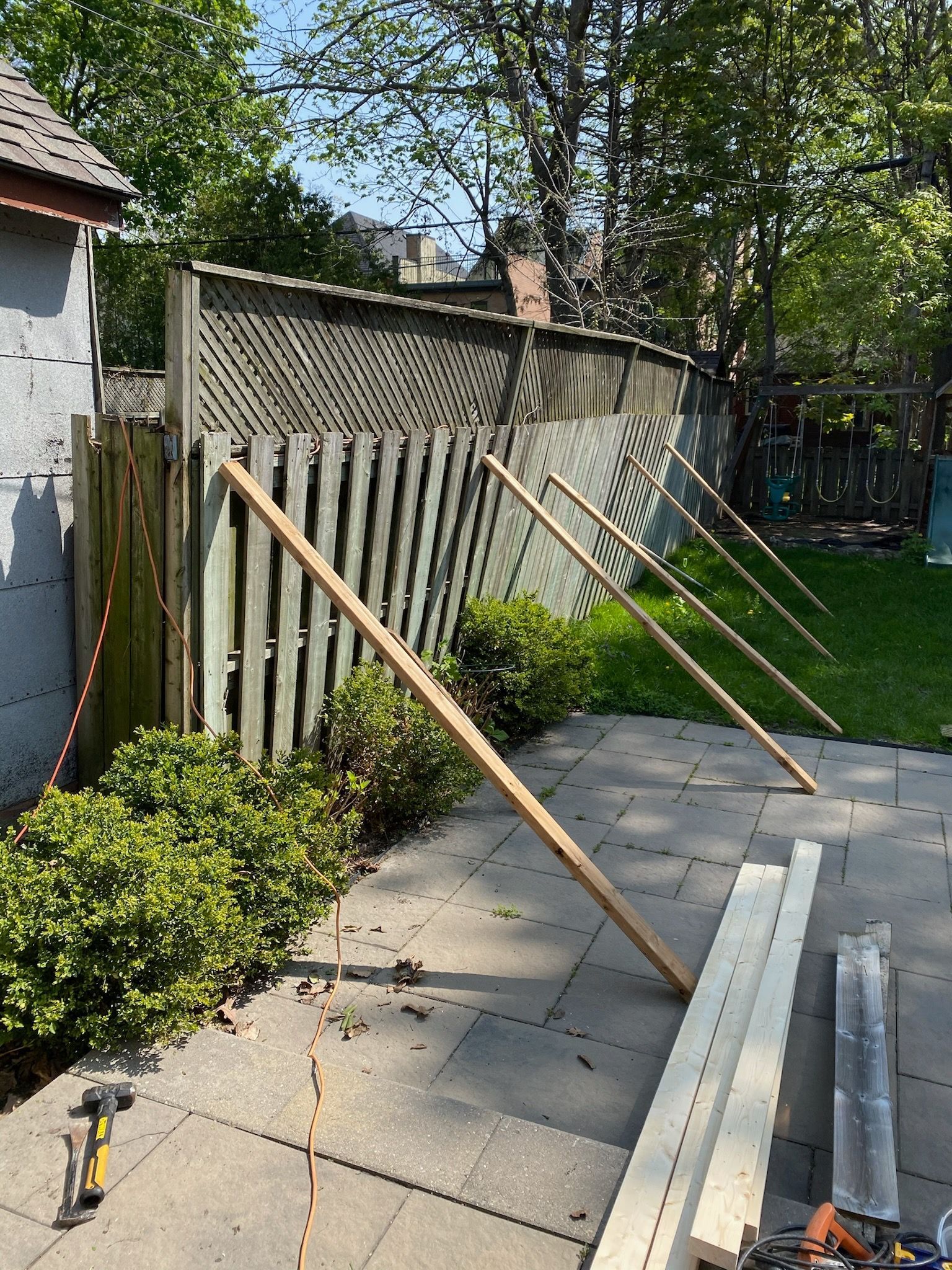 Wooden planks propped against a leaning wooden fence in a backyard, potentially for repair.