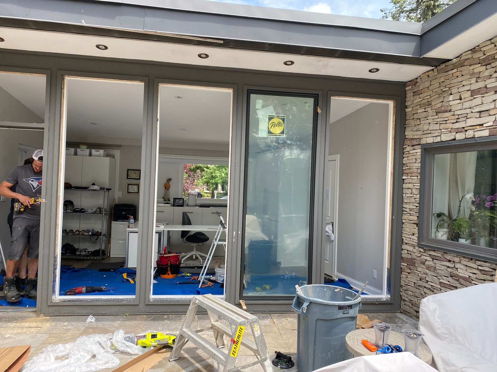 Workers installing large, gray framed glass doors. Construction setting; tools and debris visible.