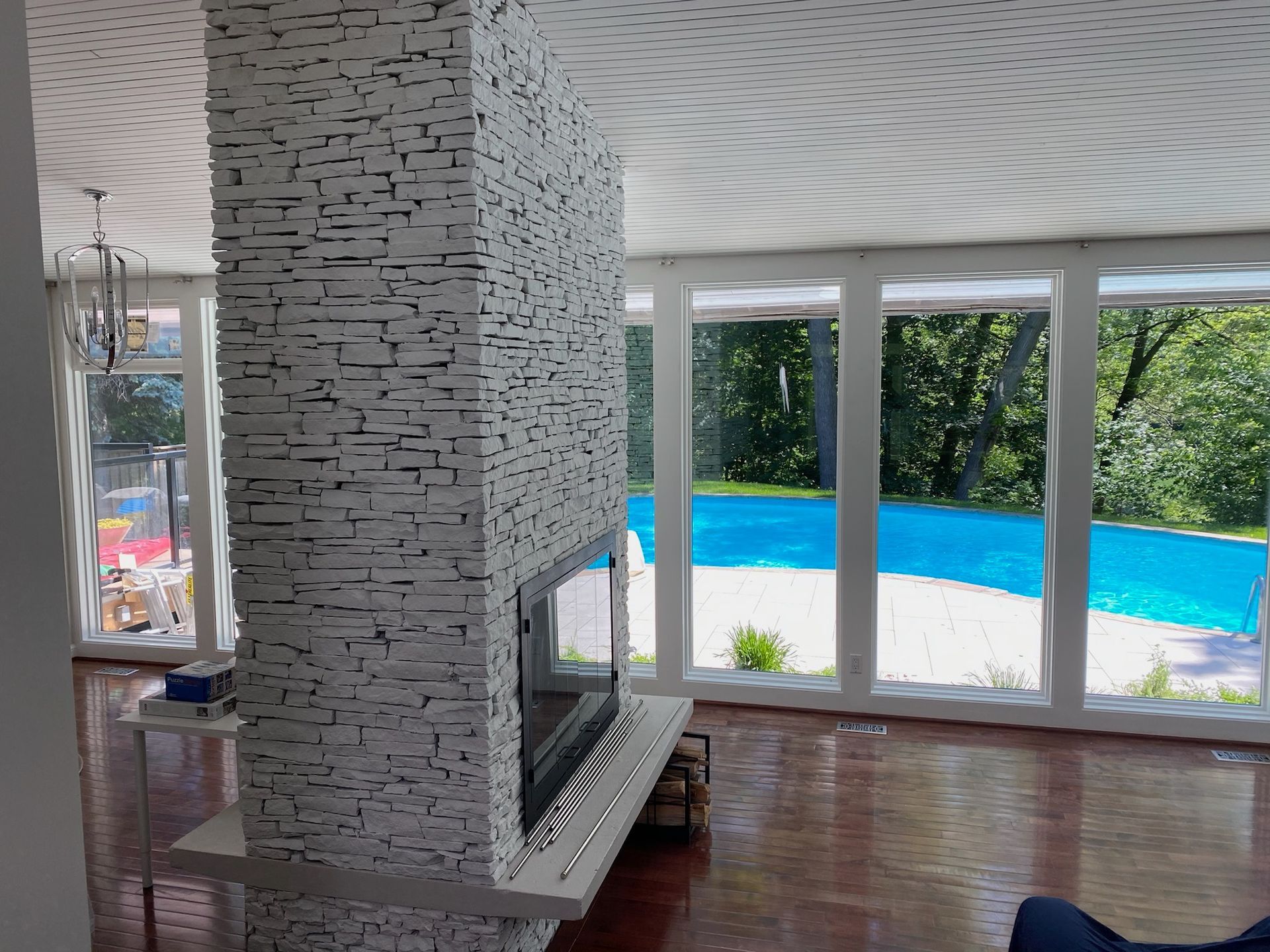 Fireplace with stone facade inside a room, with a pool visible through large windows.