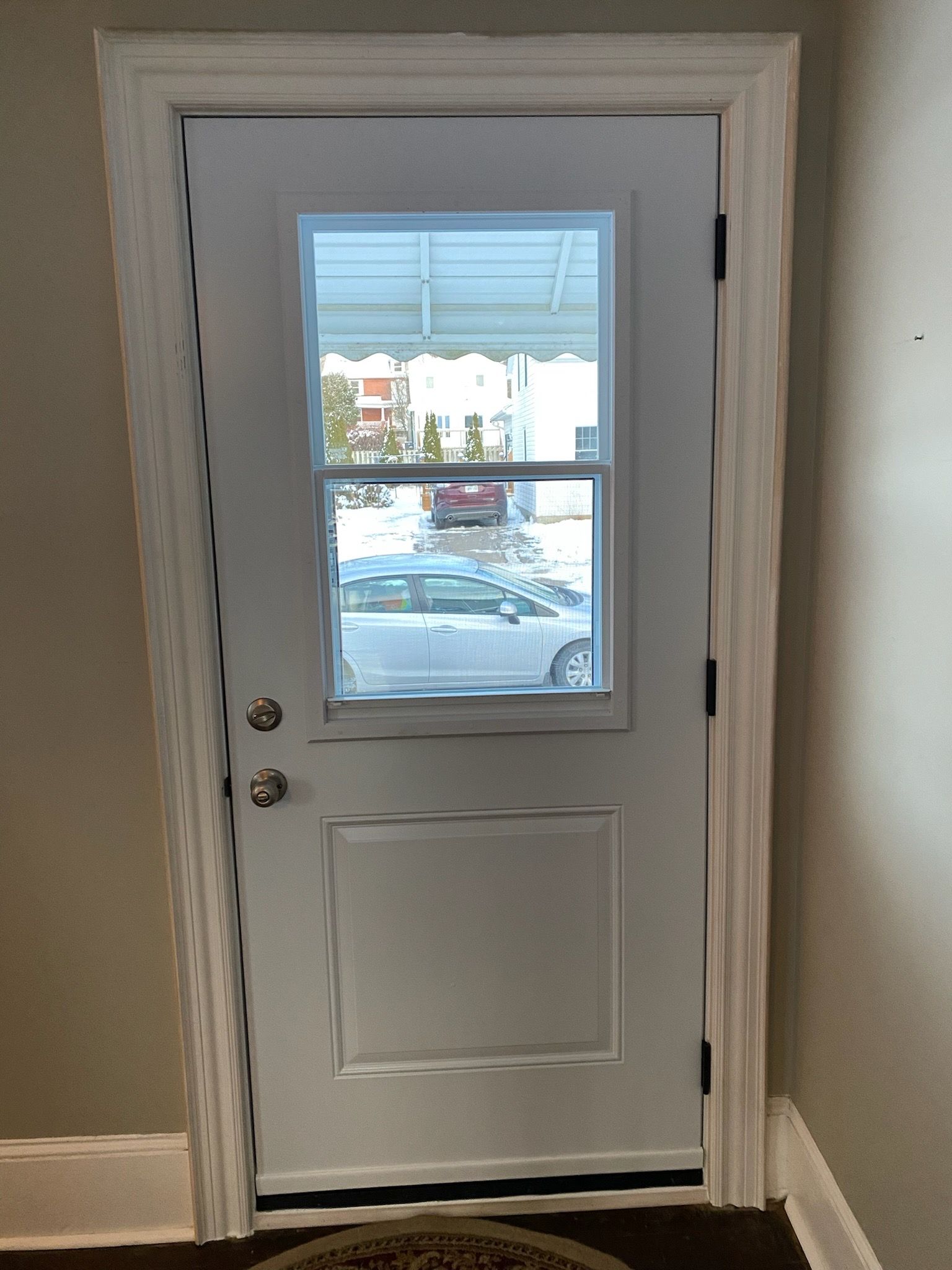 White exterior door with window, set in white trim. View to outside, showing street and cars.