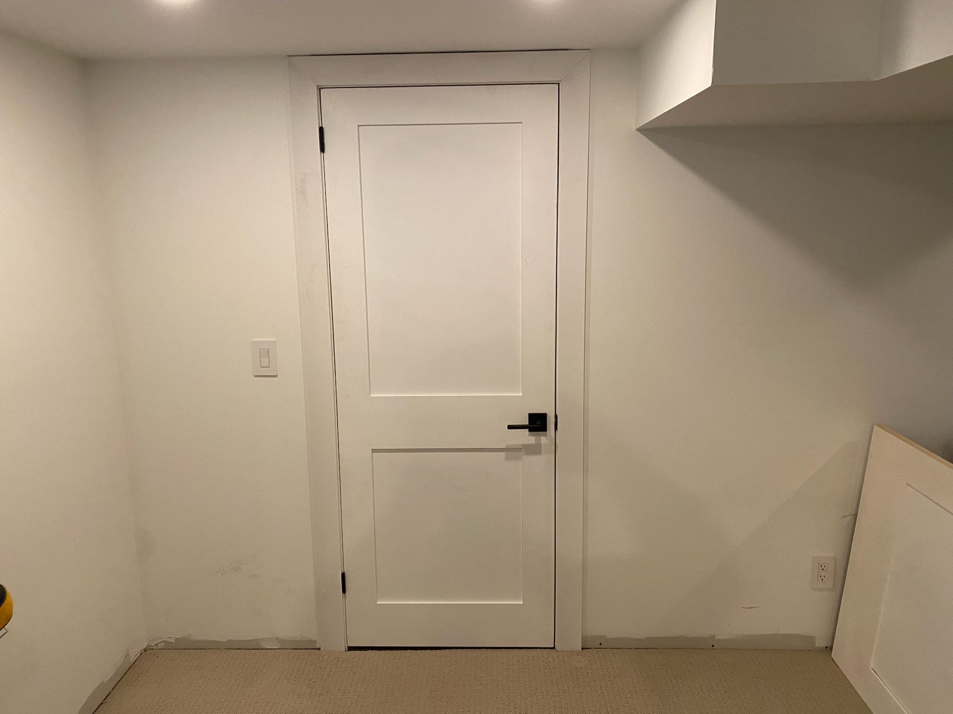 White interior door in a room with white walls, black handle, and carpeted floor.
