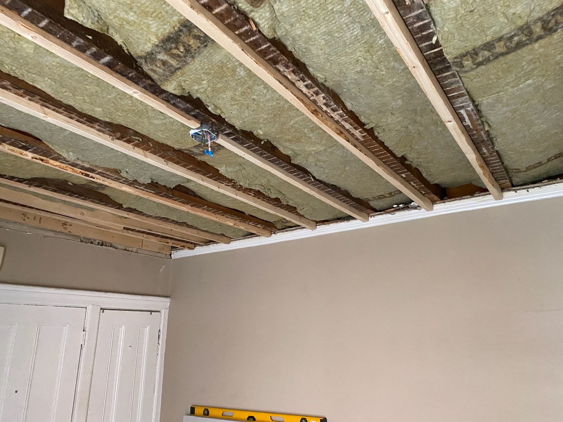 Ceiling insulation between wooden beams, with a light fixture, and drywall.